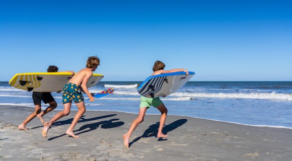3 young men running to the ocean with surfboards