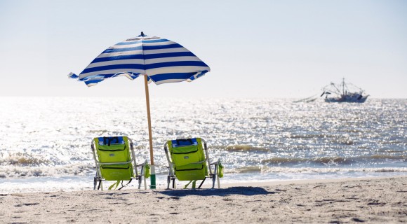 Two beach chairs and blue and white striped umbrella on beach with ocean and boat in background
