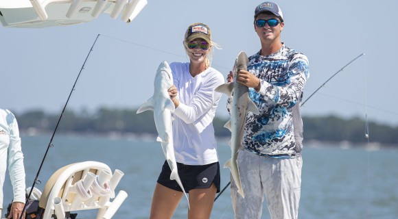 man and woman holding sharks they caught on a charter boat