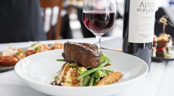 steak on top of mashed potatoes and vegetables with wine glass and wine bottle