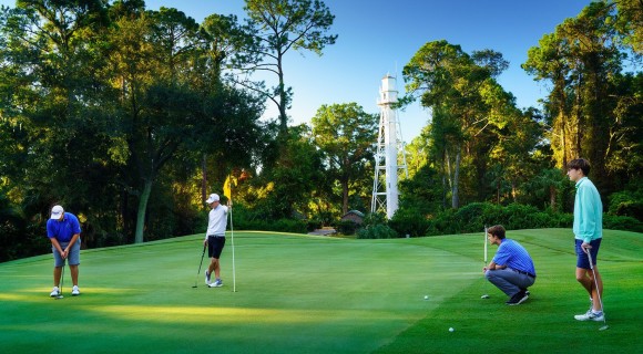 Group of four golfers putting on green with lighthouse in background