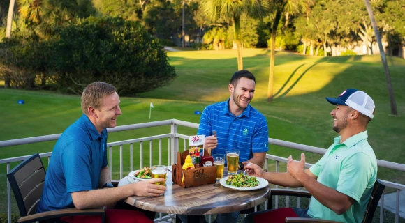 Three golfers eating lunch outside.