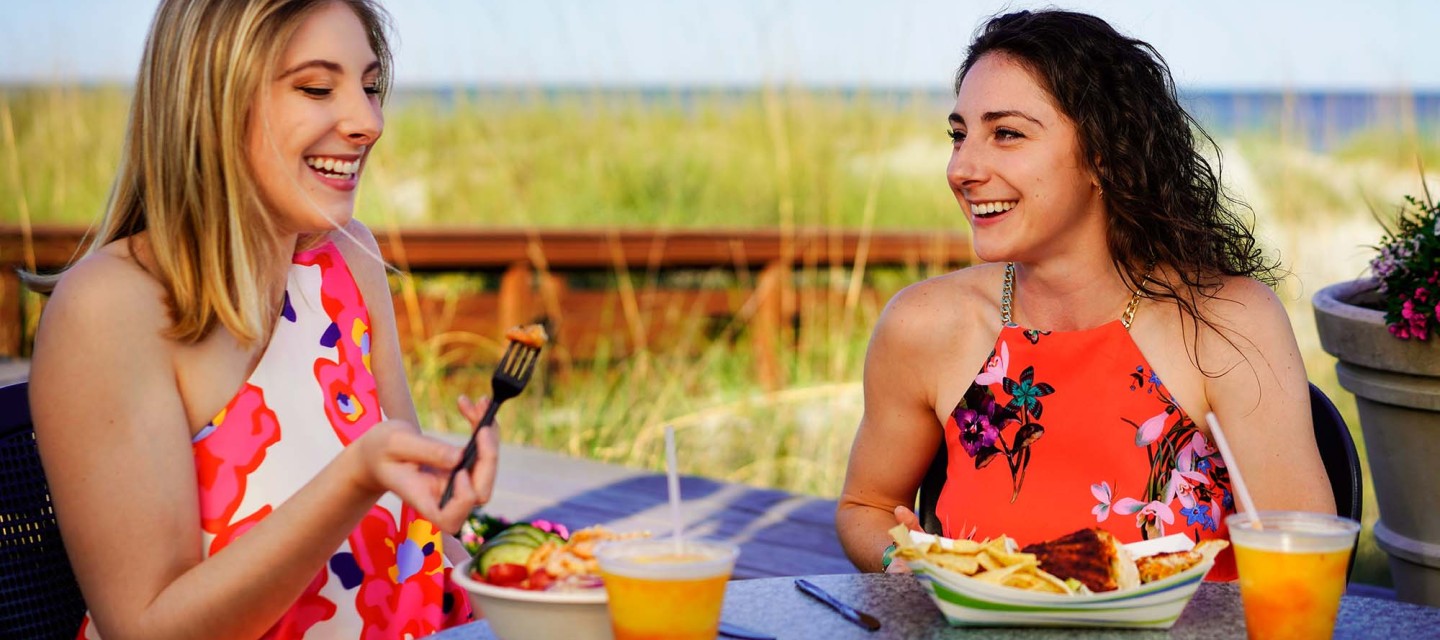 two women laughing eating dinner and drinks on the oceanfront deck of The Dunes House
