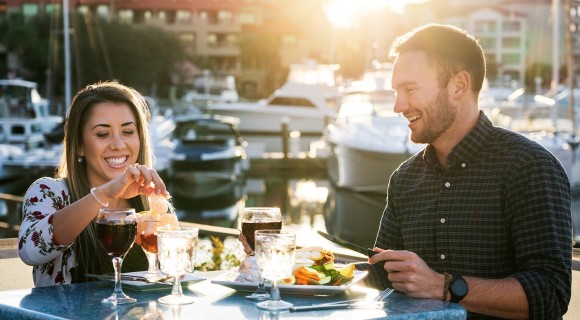 Young couple dining alfresco alongside a marina and enjoying wine and seafood.