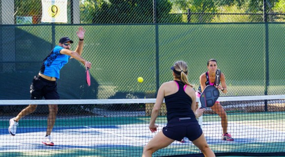Three people playing pickleball on outdoor court