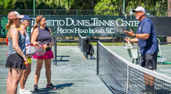 Tennis pro instructing three people during a tennis lesson on an outdoor court