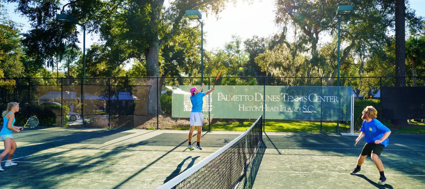 Three people playing tennis outside.