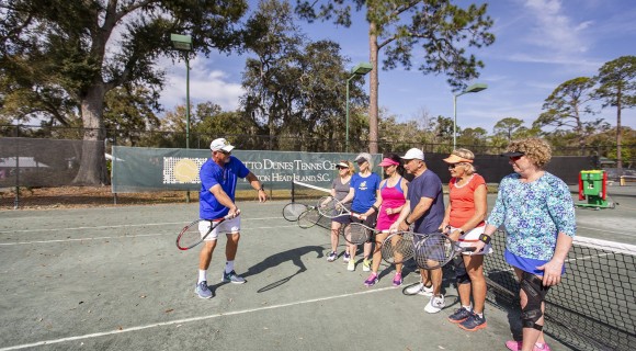 Tennis pro instructing six people during a tennis lesson on an outdoor court
