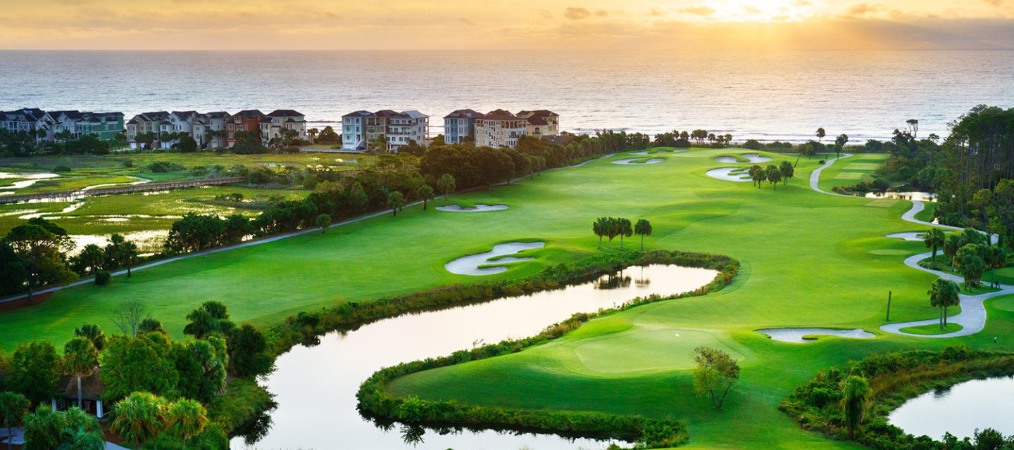Aerial view of golf course at sunrise with ocean in background