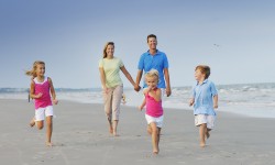 Family of five with three young children walking along beach and laughing